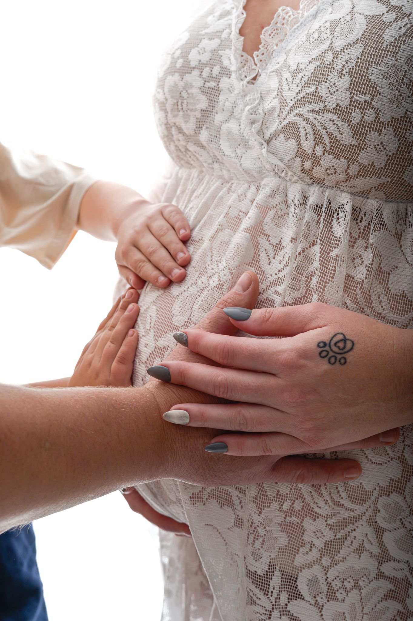 Pregnant woman with red hair poses in a flowing beige chiffon maternity gown against a neutral studio backdrop.
