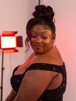 Woman in black sequin off-shoulder gown poses elegantly in front of a red LED studio light.
