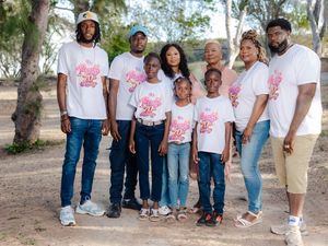 Family group photo outdoors wearing matching white graphic t-shirts, posing together among trees on a sunny day.