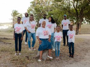 Group of people wearing matching white graphic t-shirts posing together outdoors near trees and sandy ground.