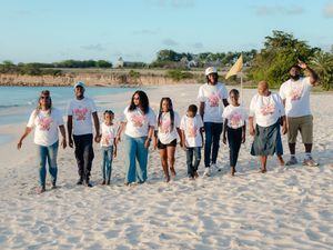 Group of people in matching white t-shirts walking on a sandy beach during a community cleanup event.