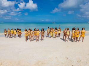 Group of women in yellow swimwear and cover-ups posing on a tropical white sand beach with turquoise water.