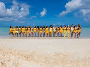 Group of women in matching yellow outfits posing on a tropical beach with turquoise water and blue sky.