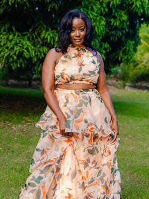 Woman in floral two-piece crop top and maxi skirt outfit posing outdoors in a lush green garden.