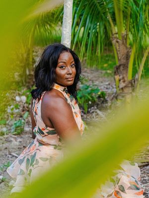 Woman in floral dress posing among tropical palm trees in a lush green garden setting.