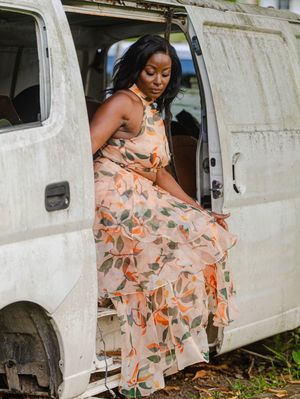 Woman in floral peach maxi dress posing in doorway of vintage white van outdoors.