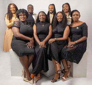 Group of nine people posing together in matching black outfits for a formal professional group portrait photo.