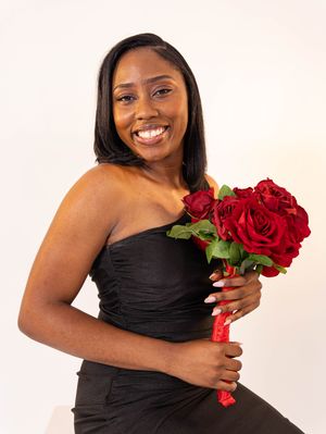Smiling woman in black strapless dress holding red roses bouquet, posing against white background.