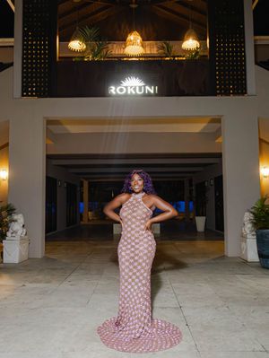 Woman in patterned halter gown poses at night outside Rokuni venue entrance with warm ambient lighting.