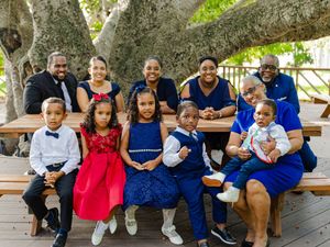 A joyful multigenerational family poses together outdoors at a picnic table, dressed in blue and red formal attire.