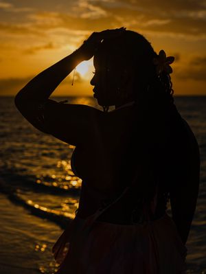 Silhouette of a woman with a flower in her hair standing on a beach at golden sunset.