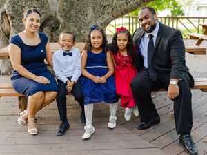 Happy family of five posing on a wooden bench outdoors, dressed in formal attire for a special occasion.