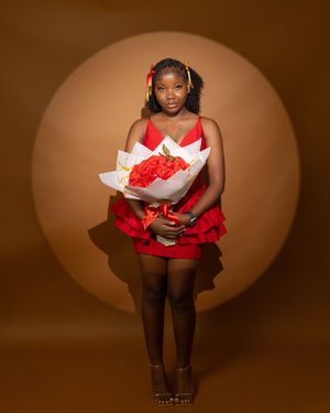 Young woman in red dress holding red rose bouquet, wearing gold hair accessories, posing in studio with circular backdrop.