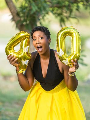 Woman in yellow skirt holding gold number 40 balloons celebrating birthday outdoors.