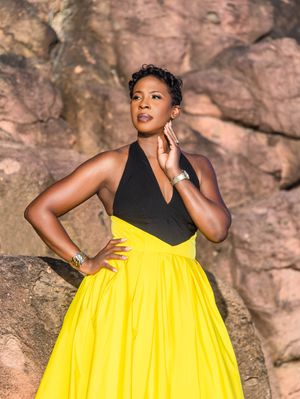 Woman in black halter top and yellow ball skirt posing gracefully against rocky background outdoors.