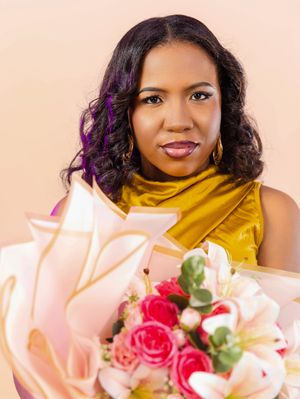 Woman in gold top holding pink floral bouquet with roses and lilies against a peach background.