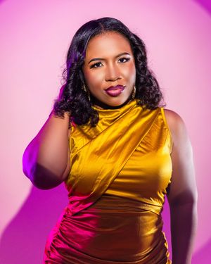 A woman in a gold satin dress poses confidently against a pink background with purple lighting.