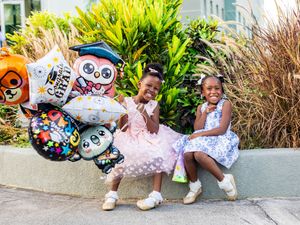 Two young girls smile with graduation balloons outdoors, celebrating a milestone achievement together.