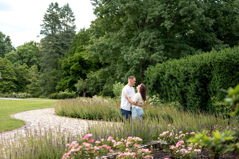 Couple walking hand in hand along a winding garden path surrounded by colorful flowers and trees.