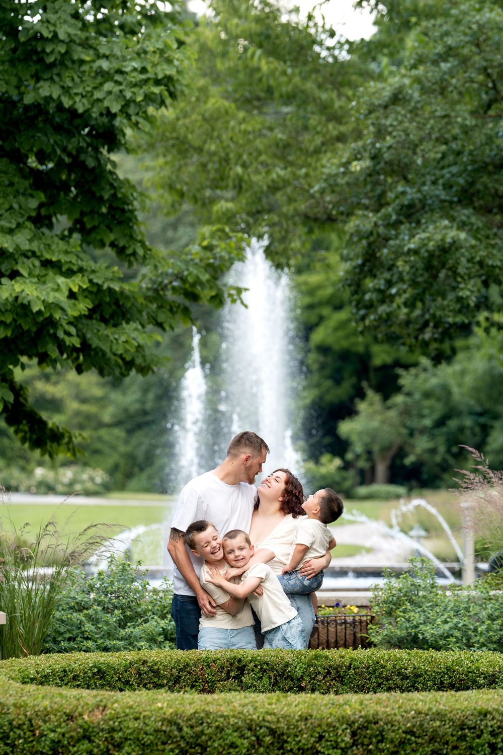 A happy family of five poses in front of a fountain in a beautiful green park.