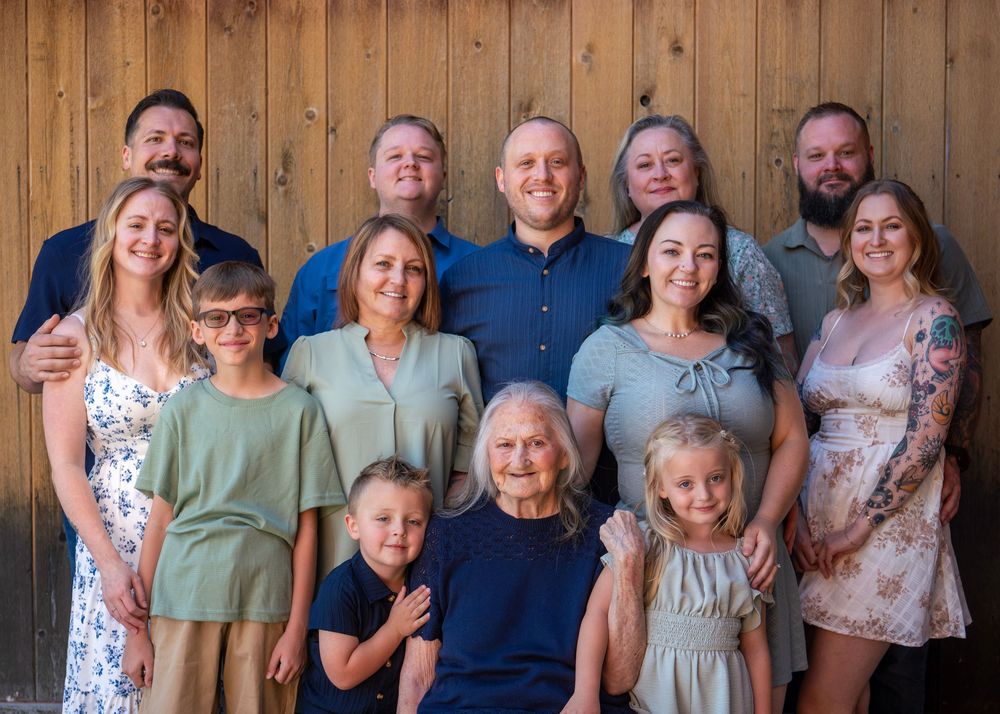 Large multigenerational family group portrait smiling together in front of a rustic wooden wall backdrop.
