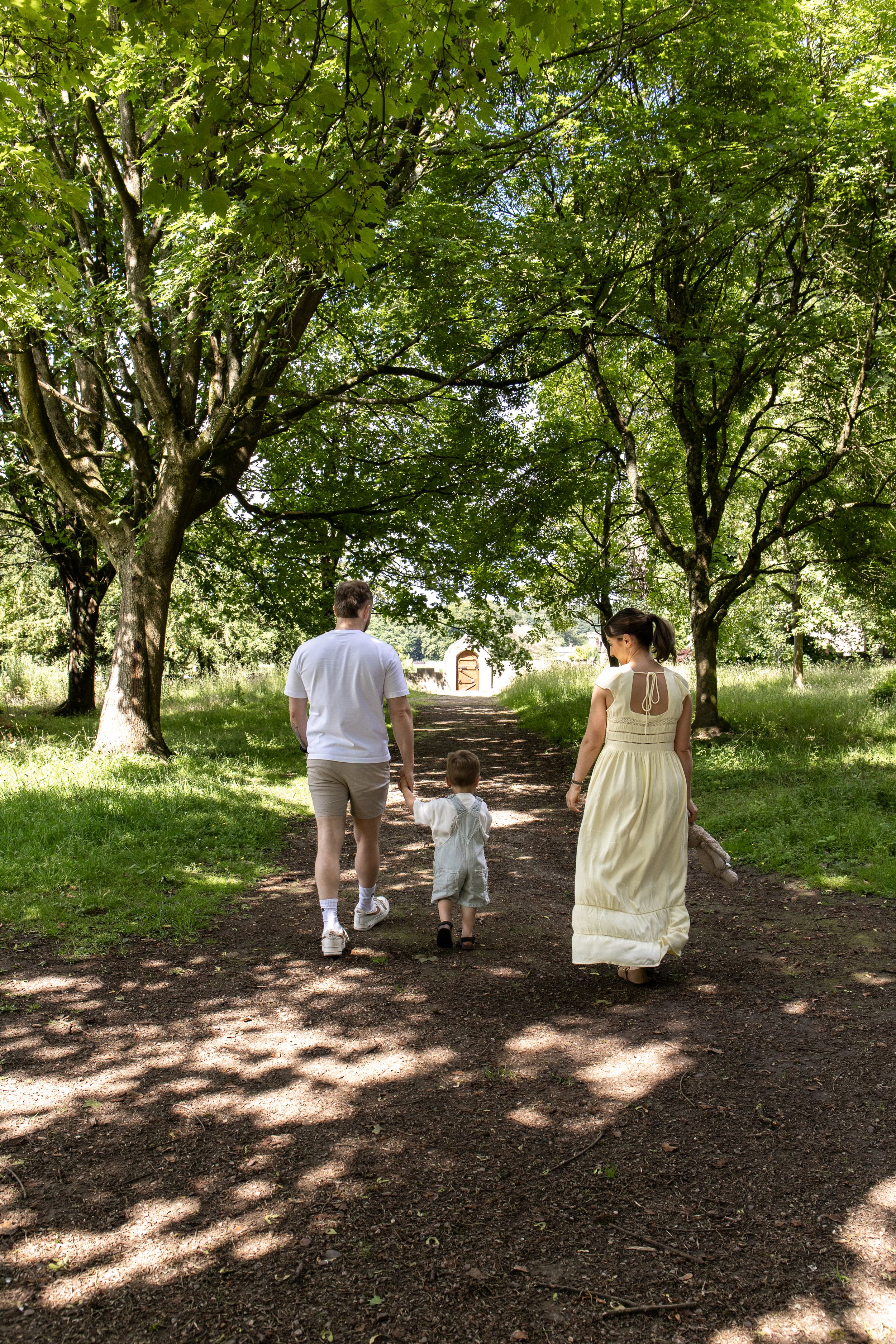 Family of three walking down a tree-lined path in a sunny park, Outdoor family photoshoot Nottingham