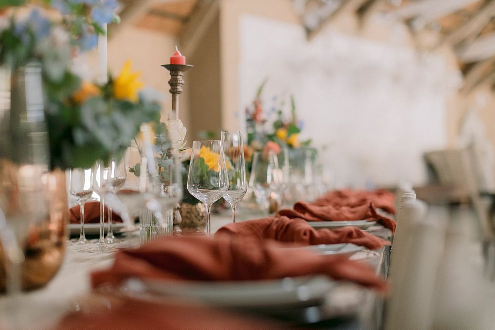 Elegant wedding reception table set with terracotta napkins, crystal glasses, candles, and colorful floral centerpieces.