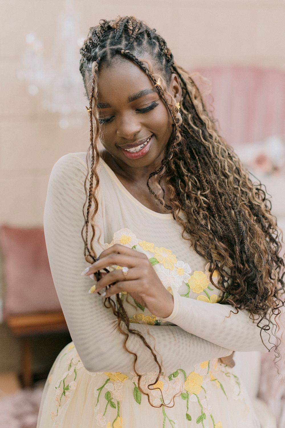 Smiling Black bride in cream floral embroidered dress with long curly braided hair, looking down gracefully.