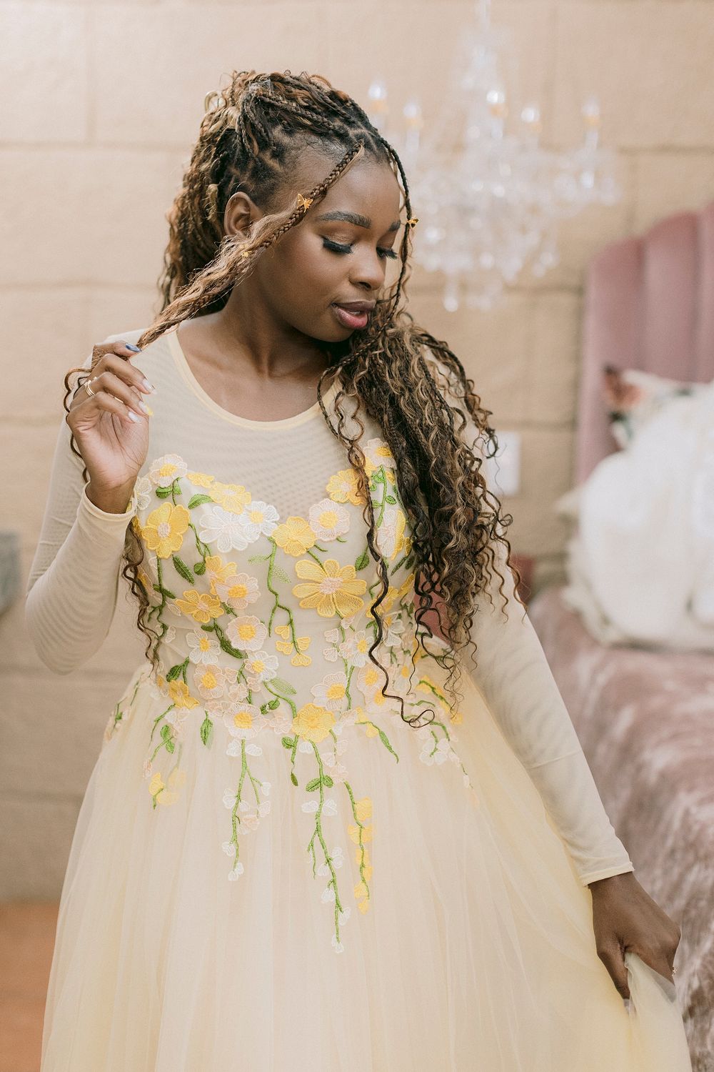 Black woman in a stunning yellow floral ball gown with long braided hair, posing in an elegant room.