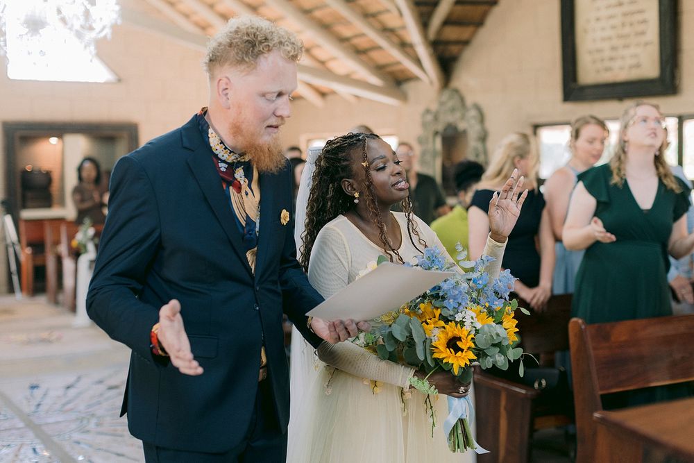 Bride and groom walking down the aisle holding sunflower bouquet at rustic wedding ceremony.