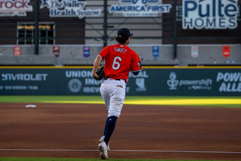 Baseball player #6 Swift runs on the field in a red and white uniform during a night game at a minor league stadium.