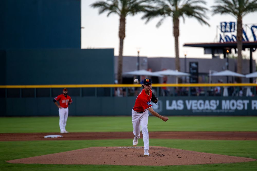 Baseball pitcher throwing at Las Vegas stadium, with teammate and palm trees visible in background.