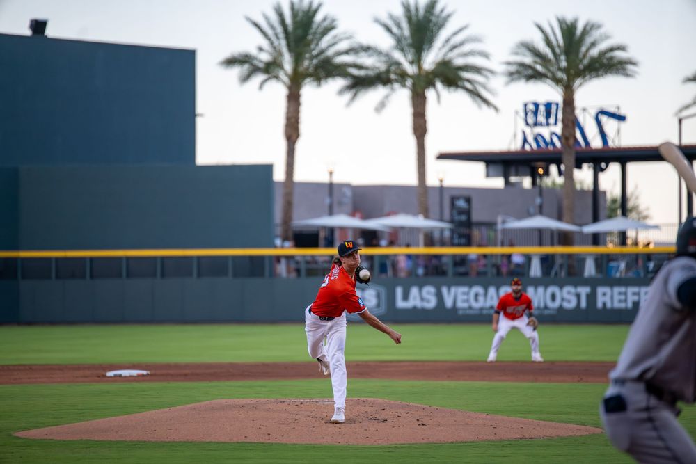 A baseball pitcher winds up to throw during a Las Vegas minor league game with palm trees in the background.