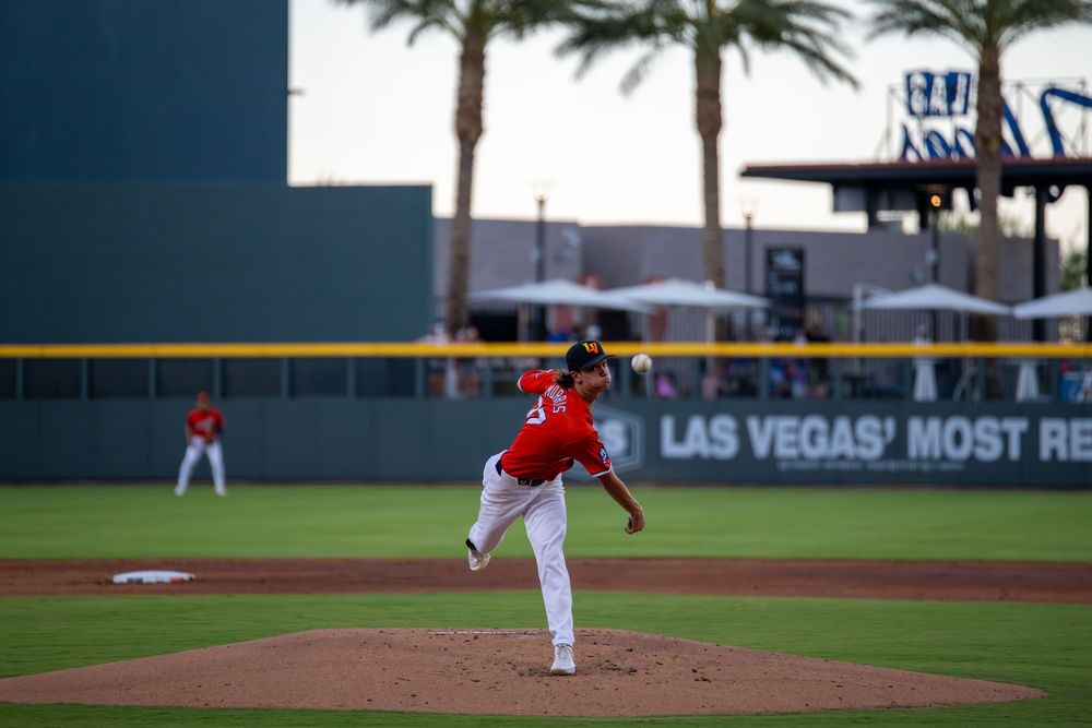 A baseball pitcher winds up to throw at Las Vegas stadium with palm trees in the background.