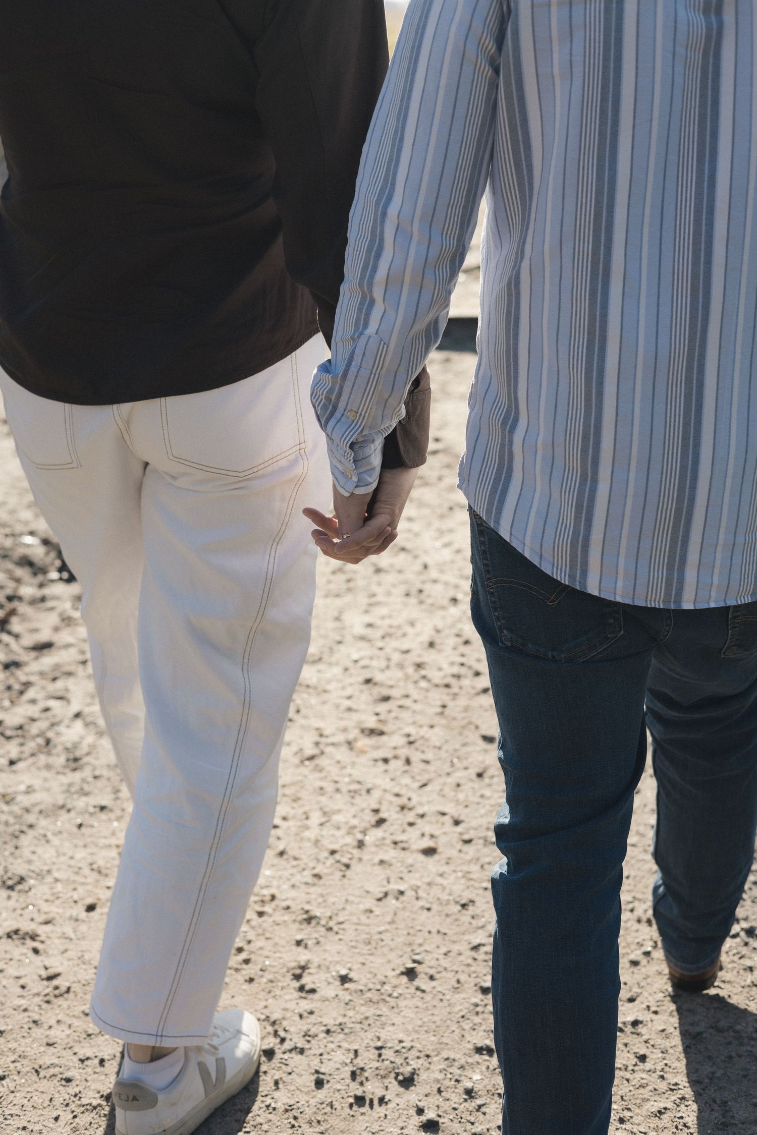 Black and white photo of a couple holding hands while walking on a path surrounded by trees.