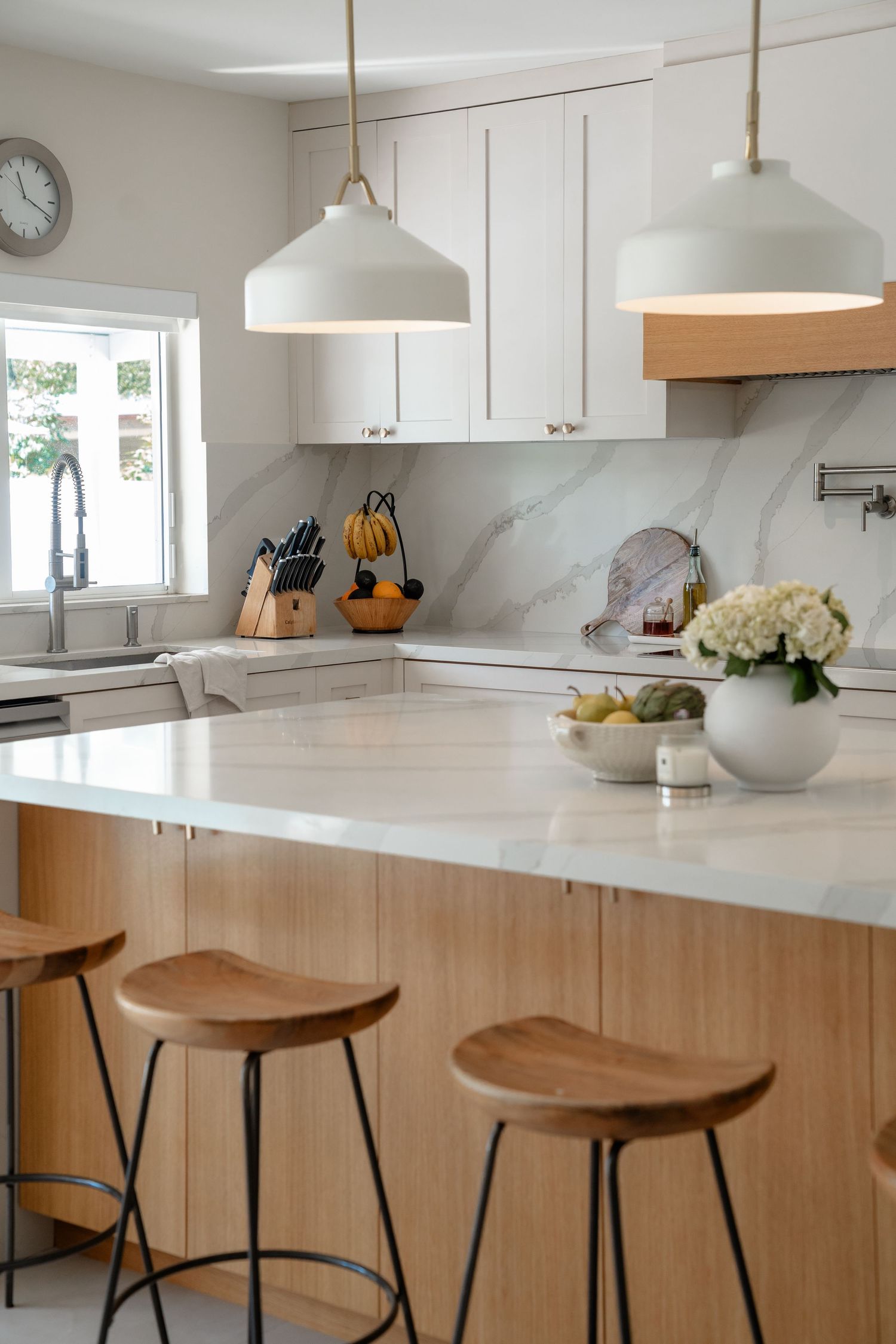 Modern white kitchen with marble backsplash, wood island, pendant lights, and bar stools.