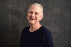 Portrait of someone in a navy shirt smiling warmly against a gray background.