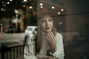 A contemplative scene through window glass of someone in a red hat and white sweater.