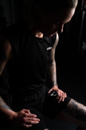 Moody low-key portrait of a tattooed person in dark athletic wear.