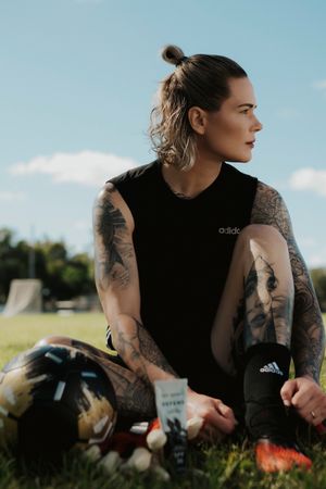 Tattooed athlete in black adidas shirt sitting outdoors with sports equipment.