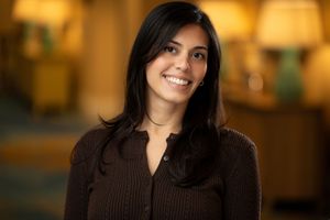 Professional headshot portrait in brown sweater with warm lighting and blurred background.