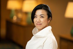 Person wearing a white turtleneck sweater smiles warmly in a softly lit indoor setting with lamps in background.