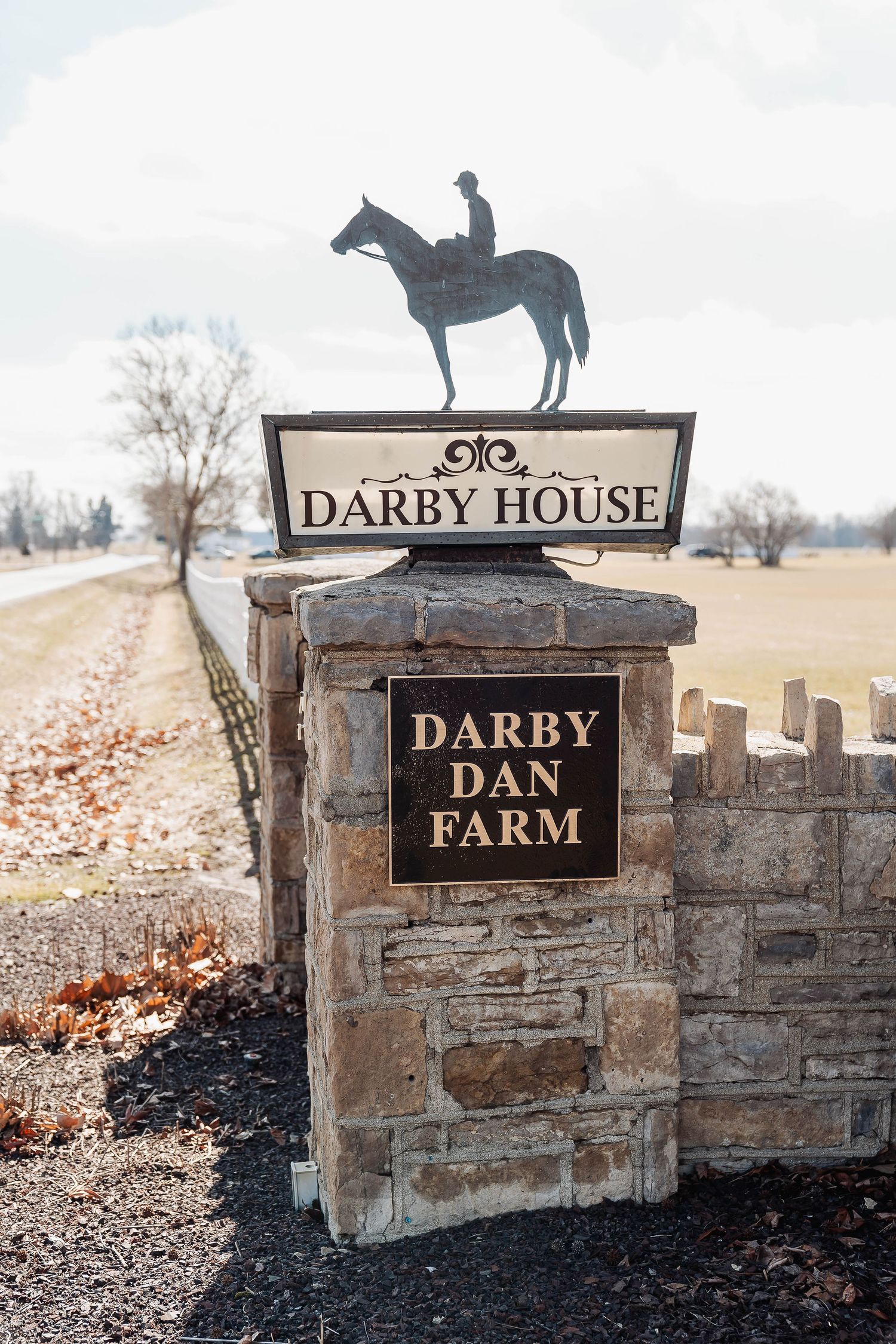 Stone entrance sign for Darby Dan Farm featuring a Darby House marker topped with a horse and rider silhouette sculpture.