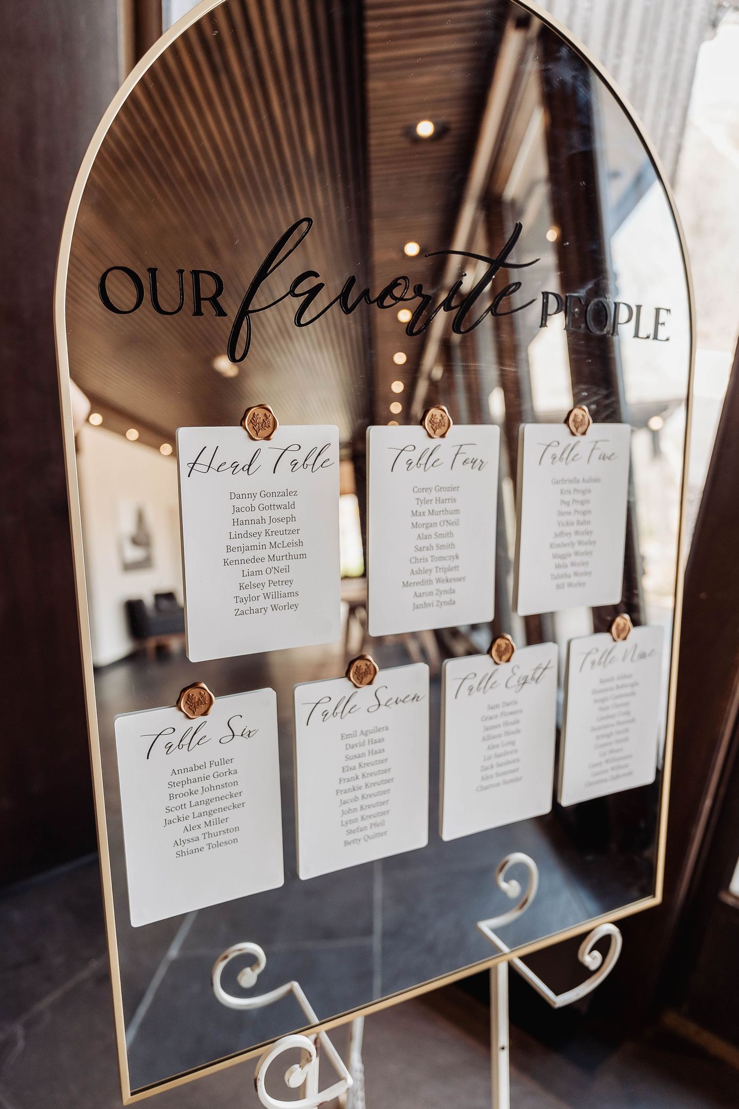Elegant wedding seating chart on a gold-framed arch mirror with white cards labeled Our Favorite People.