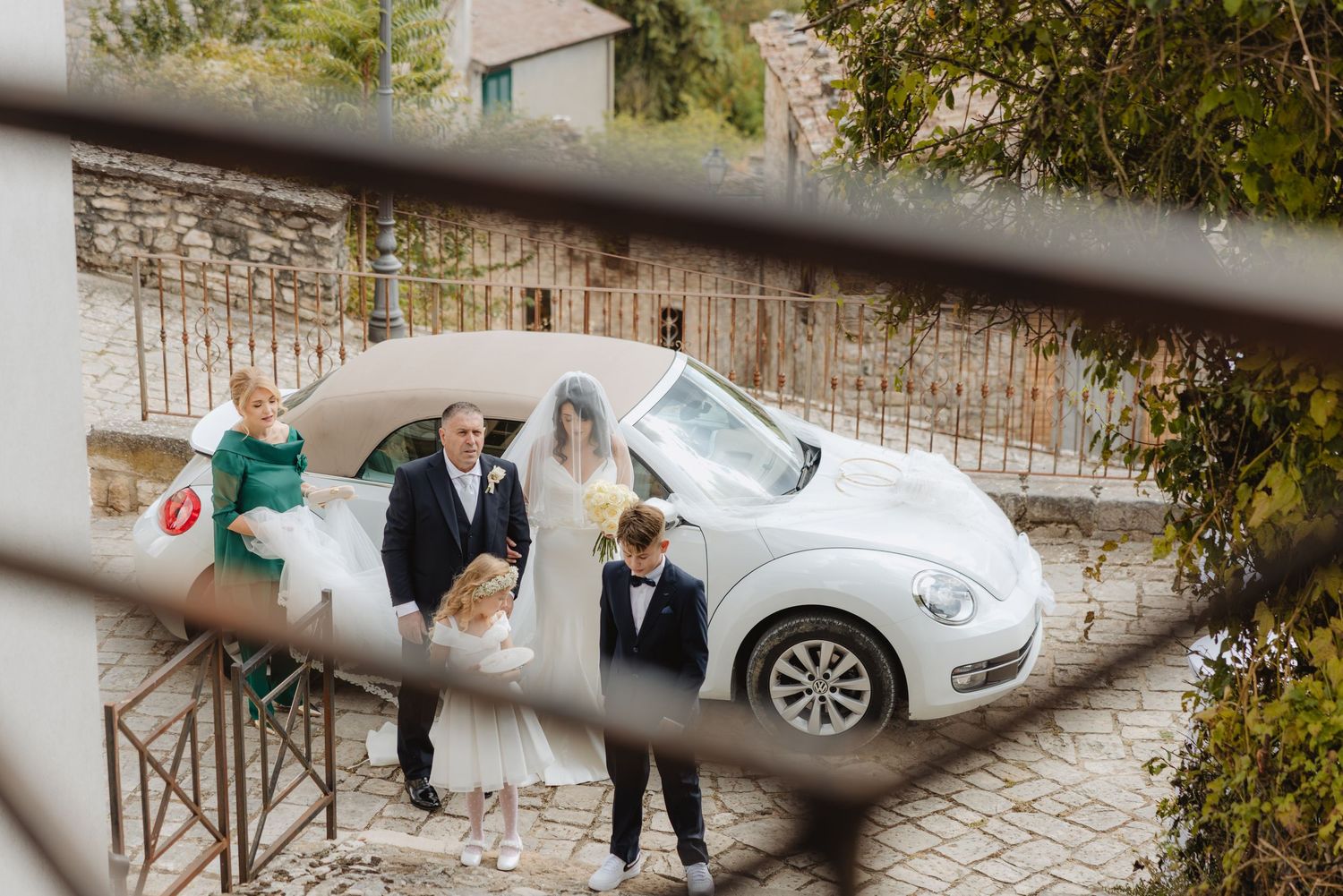 Elena arriva per la cerimonia, accompagnata dagli invitati accanto all’automobile.