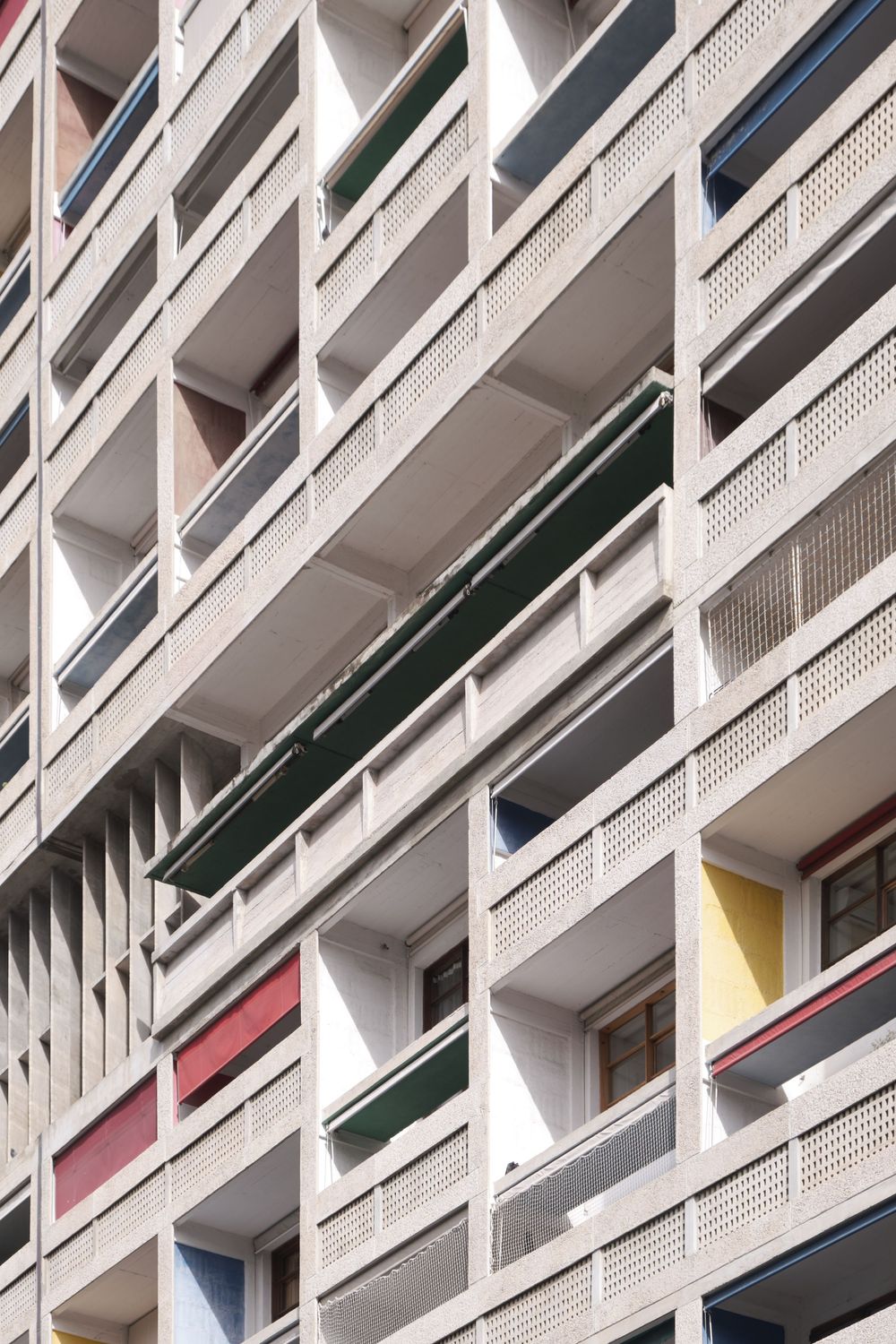Brutalist concrete apartment facade with recessed balconies, perforated railings, and colorful red, yellow, blue, and green accent panels.