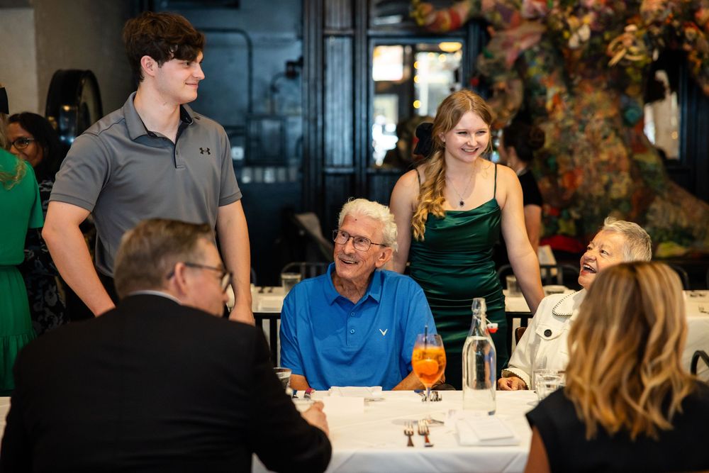 Group of people enjoying a elegant restaurant dinner, smiling and conversing around a decorated table.