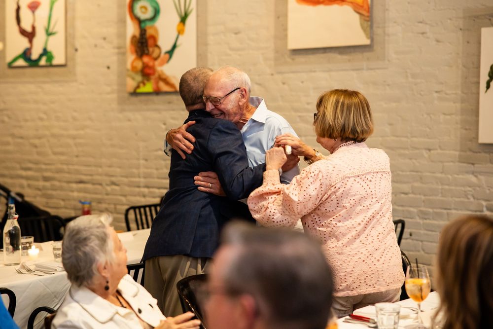 Elderly man shares warm hugs with guests at a restaurant celebration gathering.