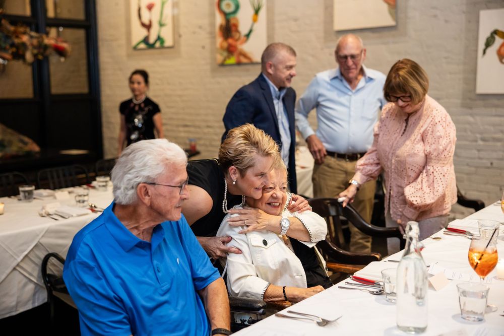People socializing at a restaurant dinner gathering, with guests greeting each other warmly at a decorated dining table.