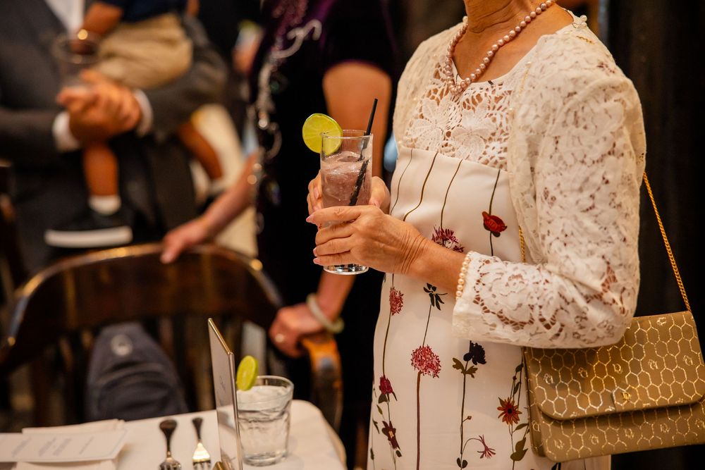 Woman in floral lace dress holding a cocktail with lime garnish at an elegant social event.